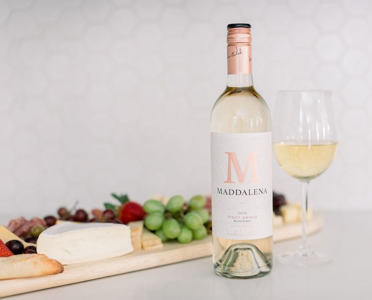 Bottle and glass of Maddalena Monterey Pinot Grigio beside a pairing board with soft cheese, grapes, strawberries, bread, crackers and charcuterie.